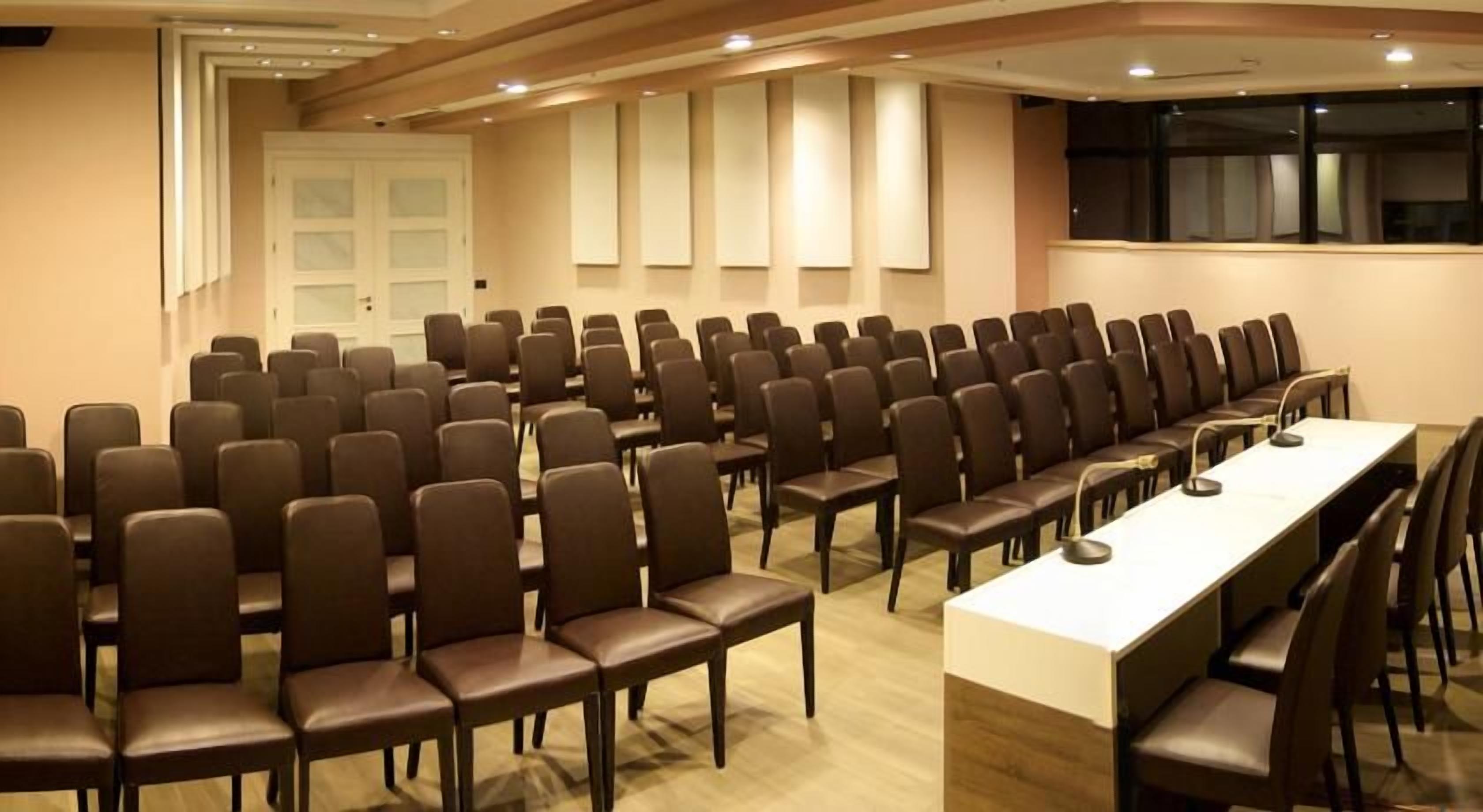 Ein Konferenzraum mit Reihen von Stühlen und einem langen Tisch, ausgestattet mit Mikrofonen.