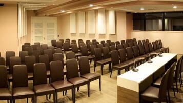 Une salle de conférence avec des rangées de chaises et une longue table, équipée de microphones.