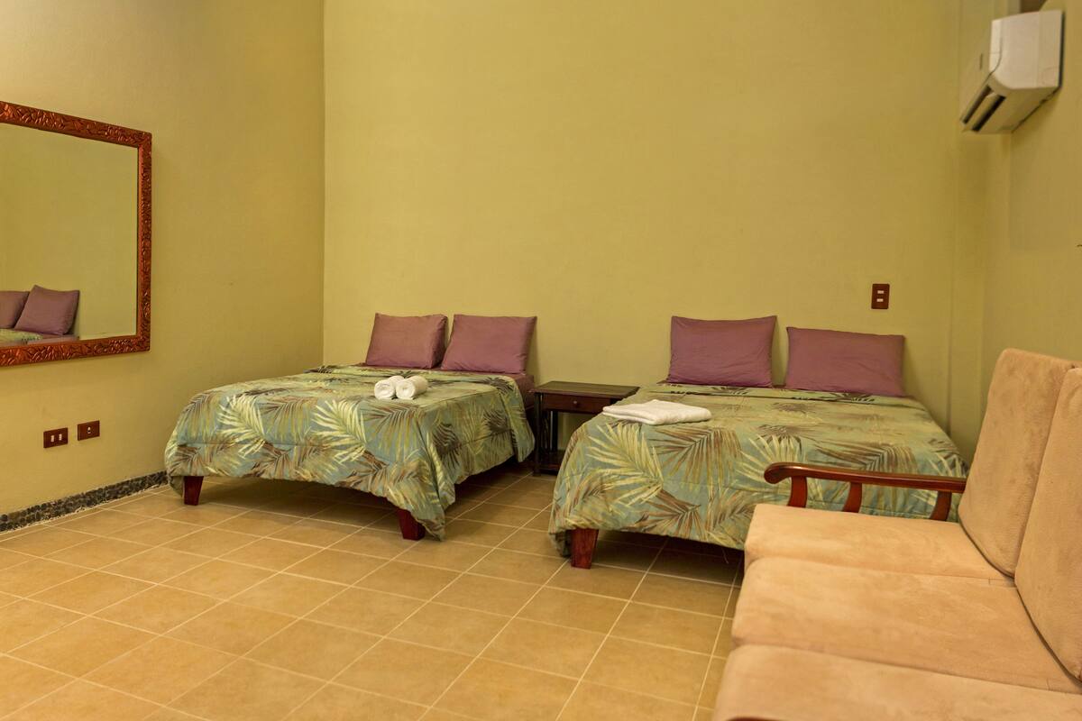 A room with two beds, each with a floral bedspread and matching pillows, a single chair, and a large mirror on the wall.