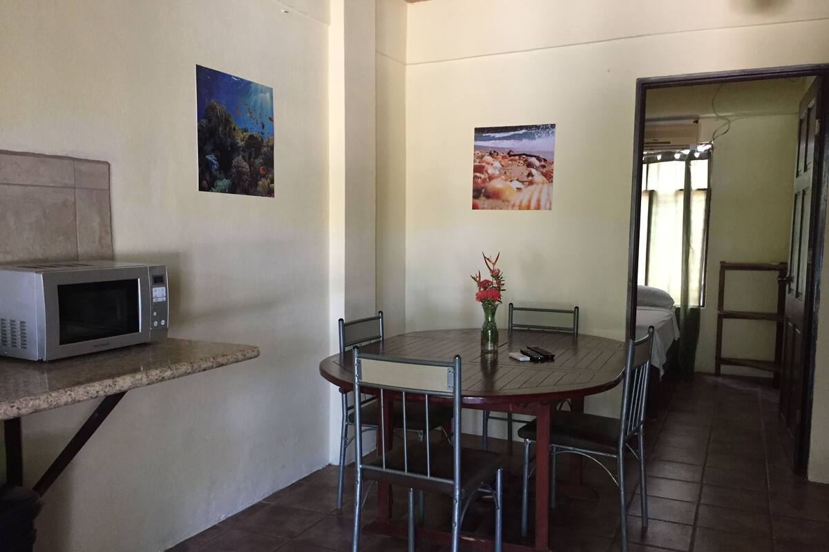 A dining area with a round table, chairs, a microwave, and two framed pictures on the wall.