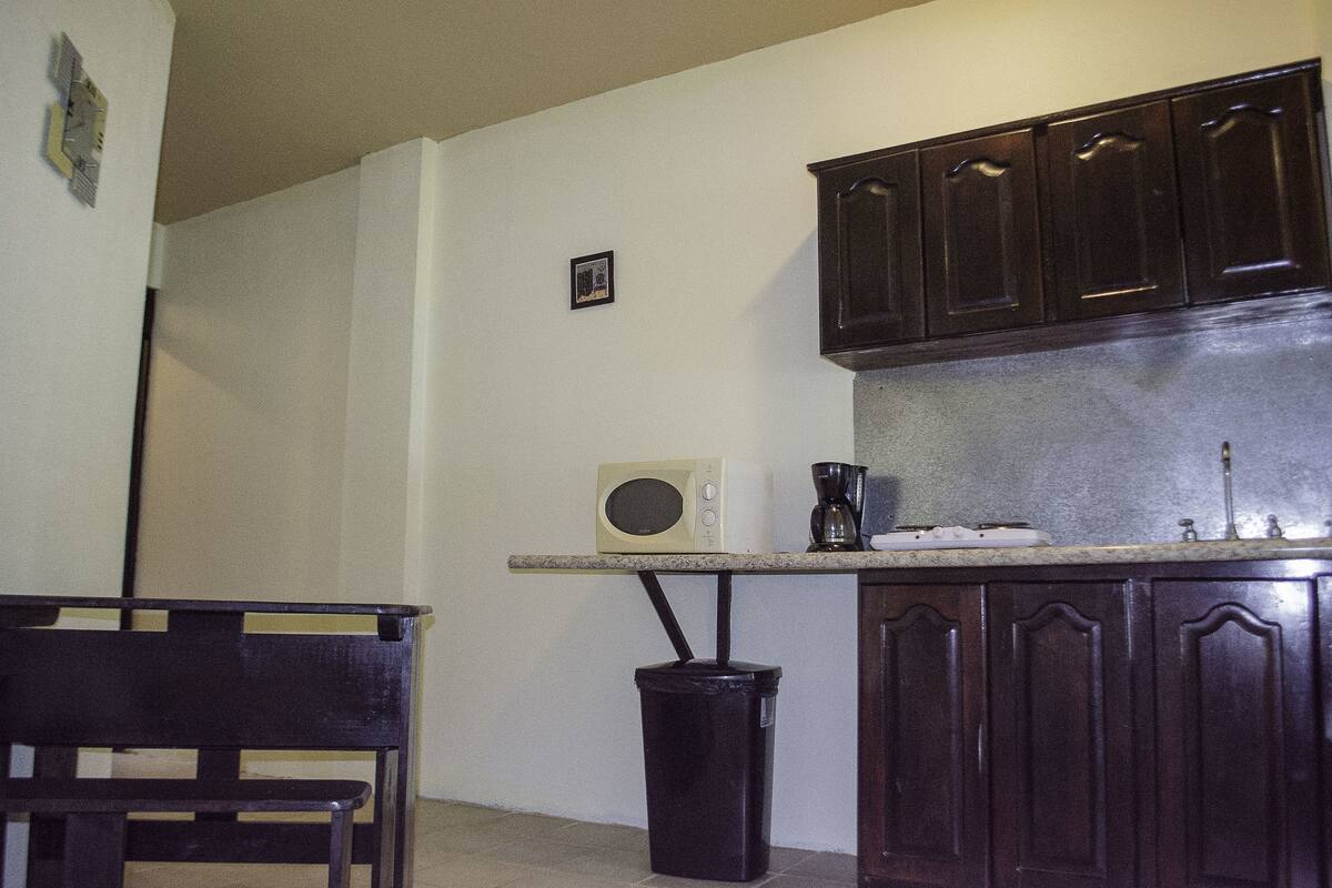 A kitchen with dark wooden cabinets, a microwave, a coffee maker, and a trash can.
