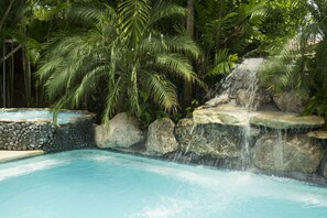 A pool with a waterfall feature surrounded by rocks and palm trees. - Apartotel Conchita (Jacó)