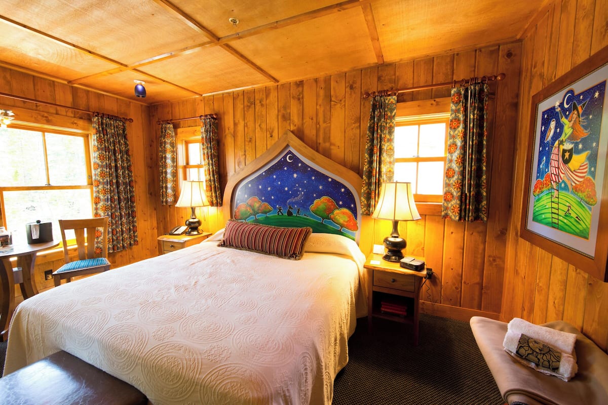 A wooden-paneled room with a bed, a desk, and a chair.