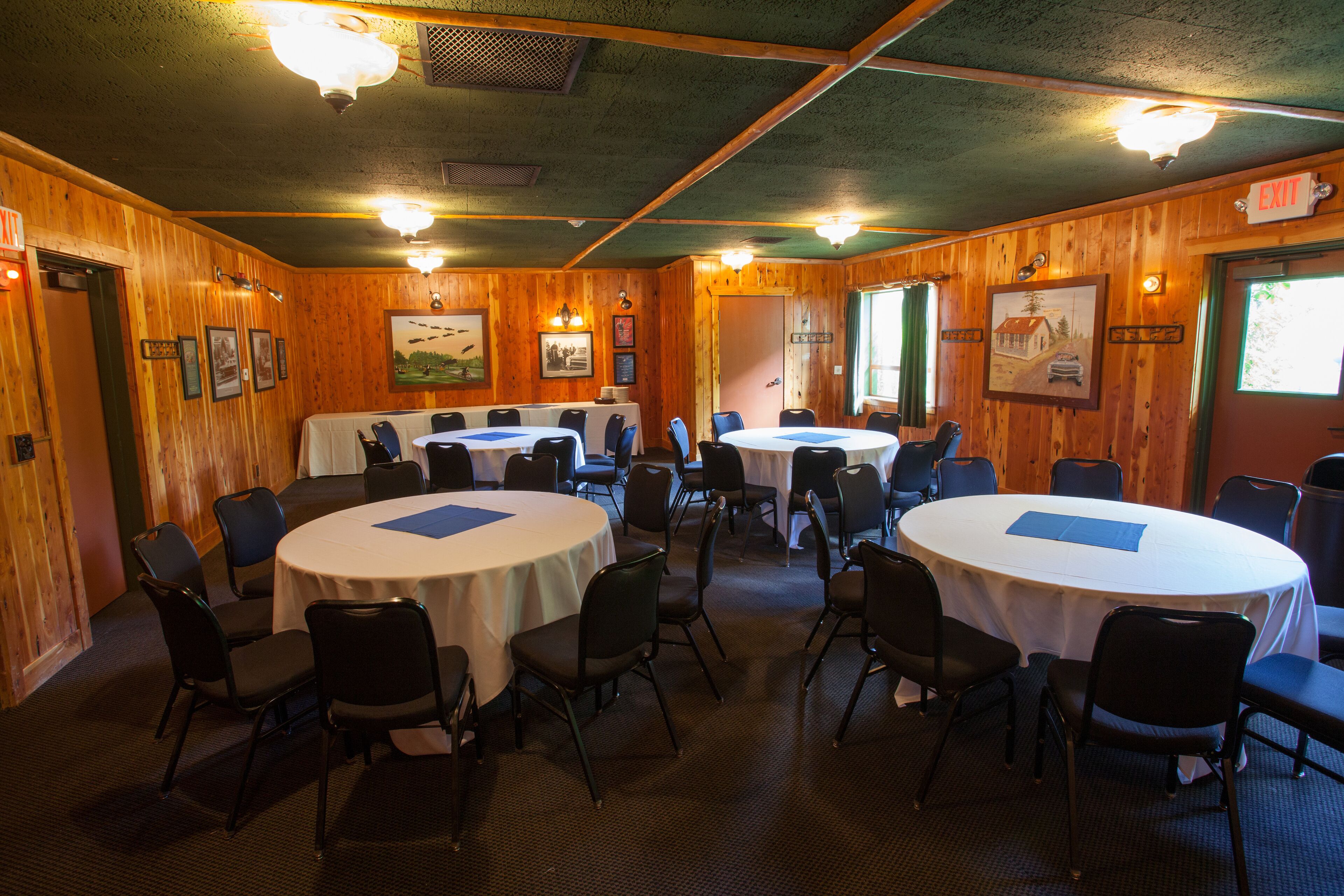 A conference room with multiple round tables and chairs, wooden walls, and framed pictures on the walls.
