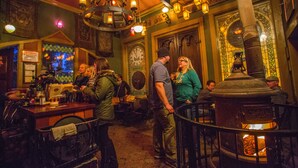A bar with a large clock, a wood stove, and a chandelier. - McMenamins Old St. Francis (Bend)