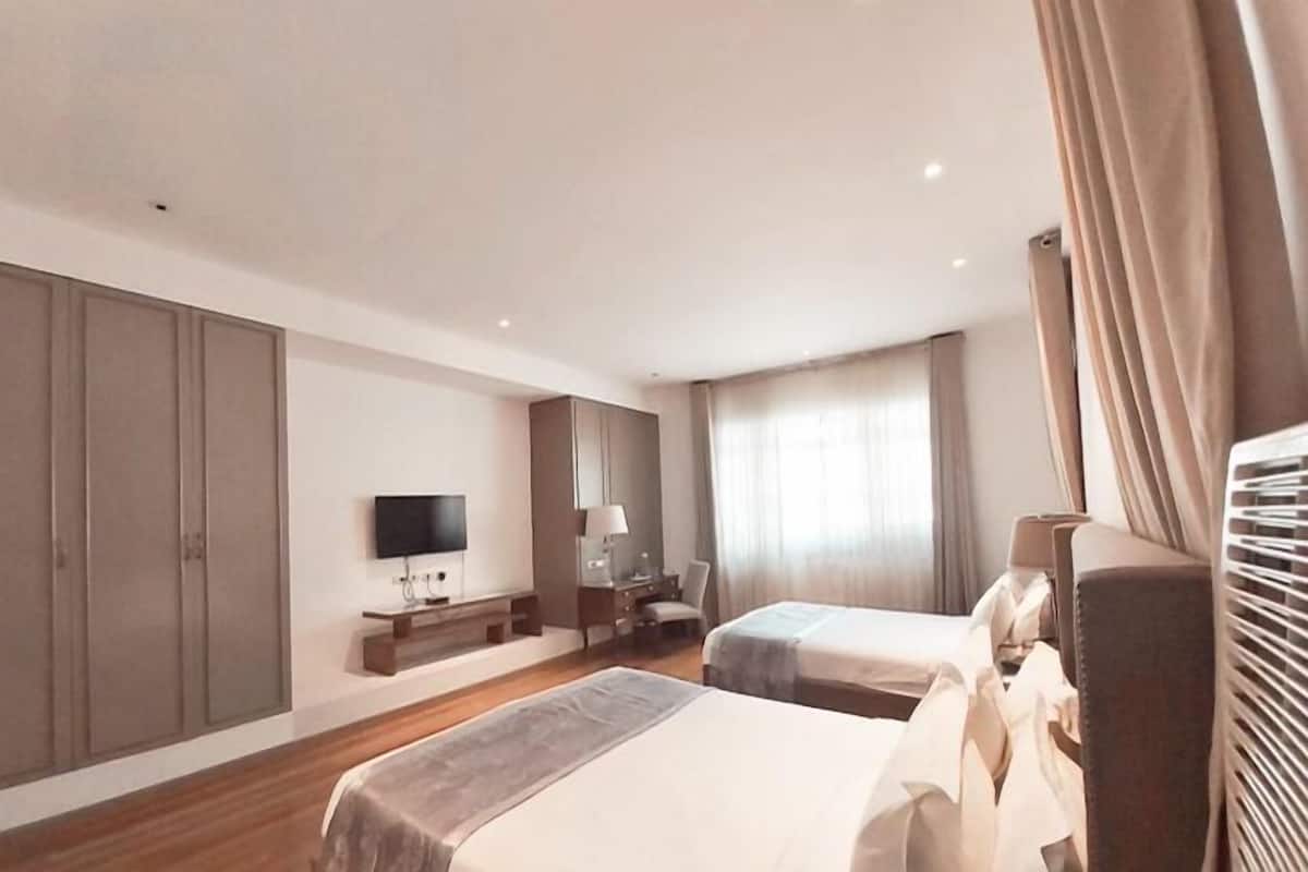 A modern hotel room with two beds, a desk, a TV, and a large wardrobe.