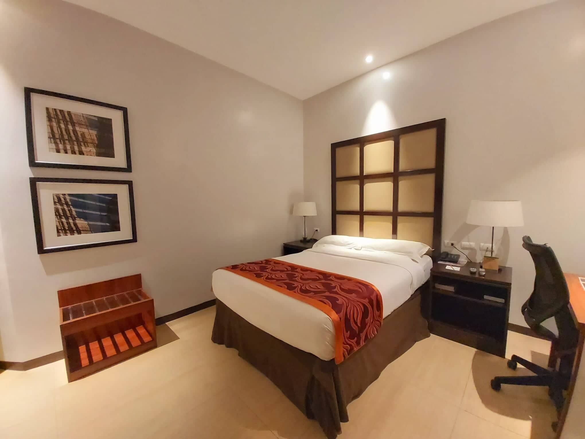 Une chambre d’hôtel comprenant un lit, deux tables de chevet, un bureau et deux lampes.