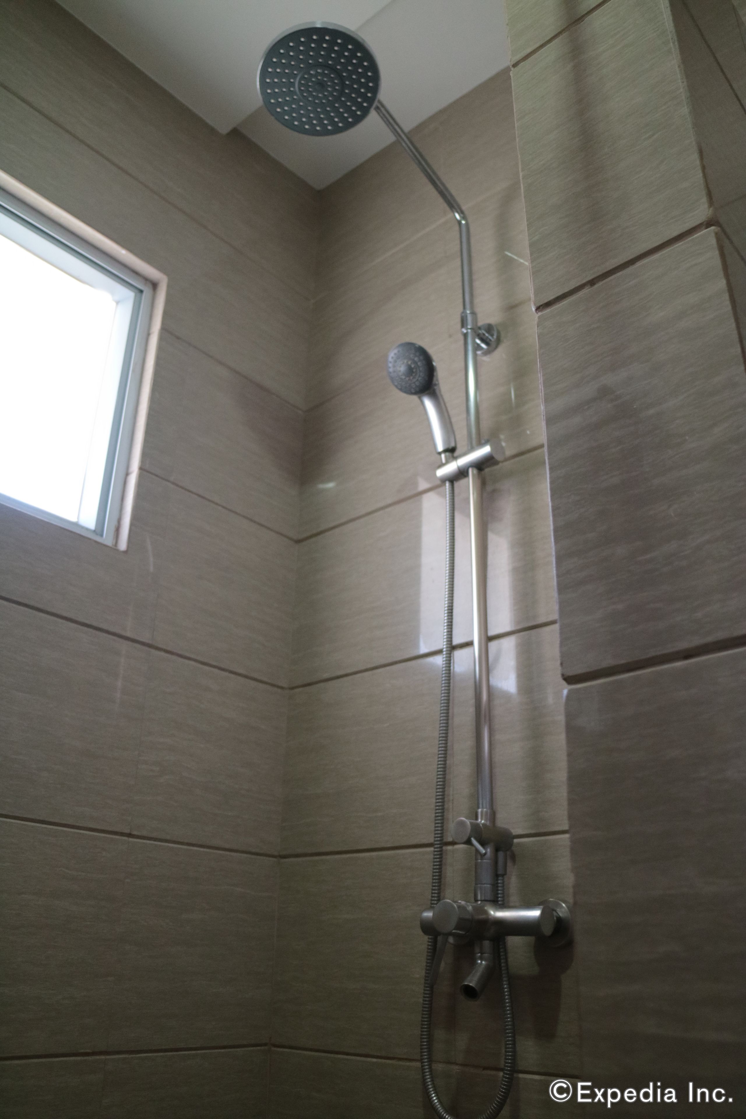 Eine Dusche mit Handbrause und Wandarmatur in einem gefliesten Badezimmer.