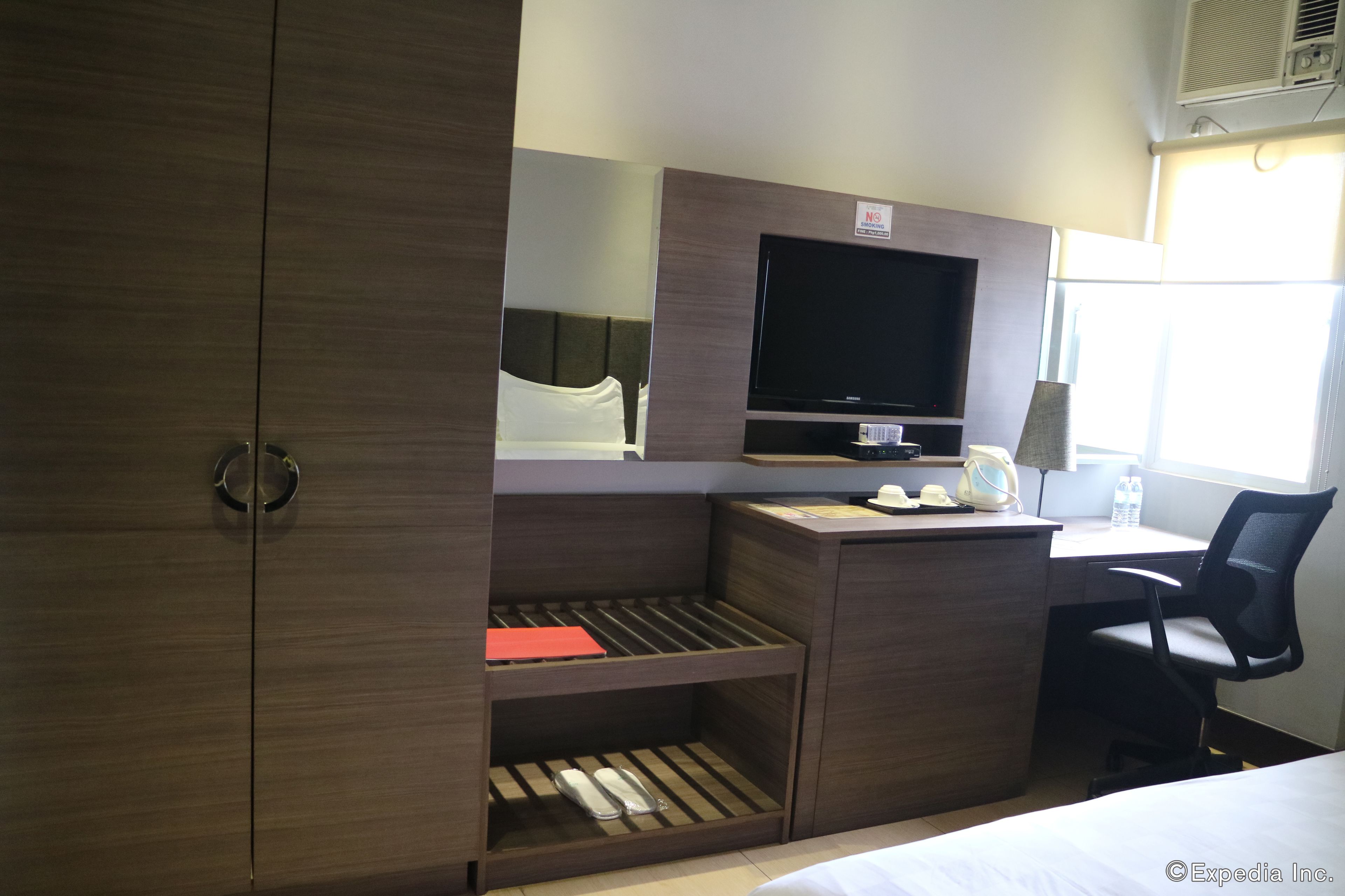 A hotel room with a bed, a desk with a computer, a chair, a TV, and a wardrobe.