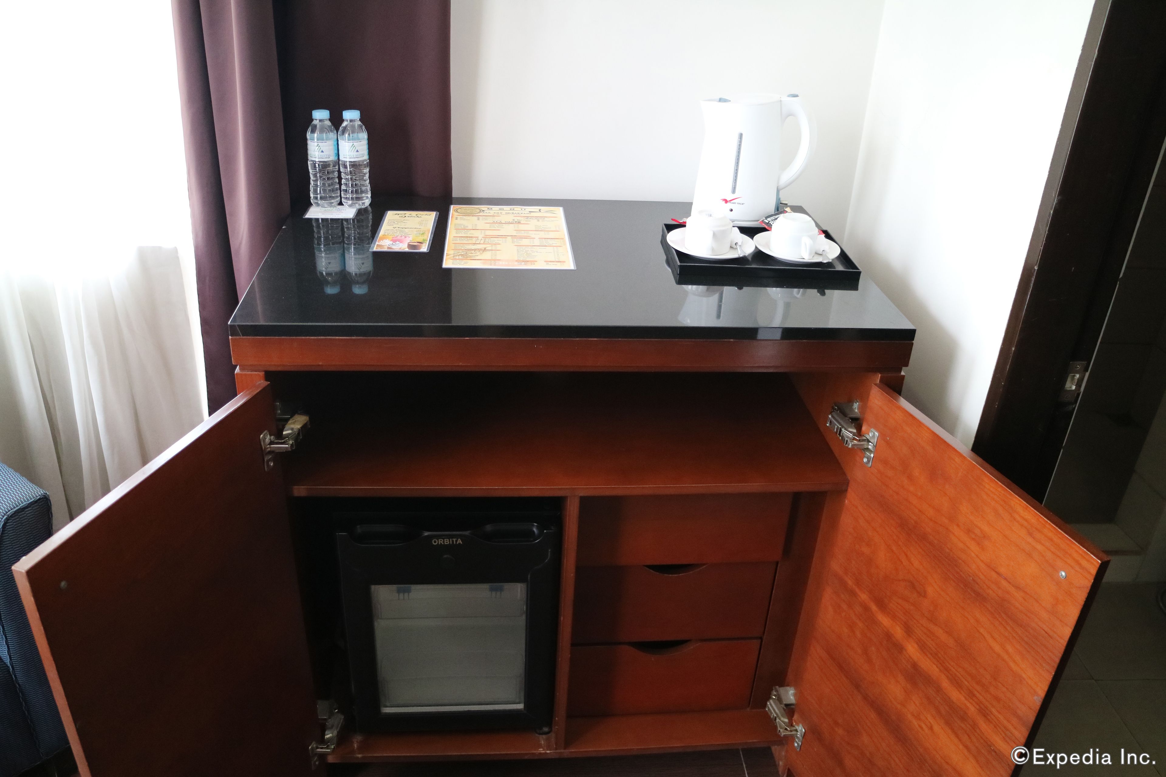 Escritorio de habitación de hotel con cafetera, botellas de agua y un menú.