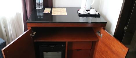 Escritorio de habitación de hotel con cafetera, botellas de agua y un menú.