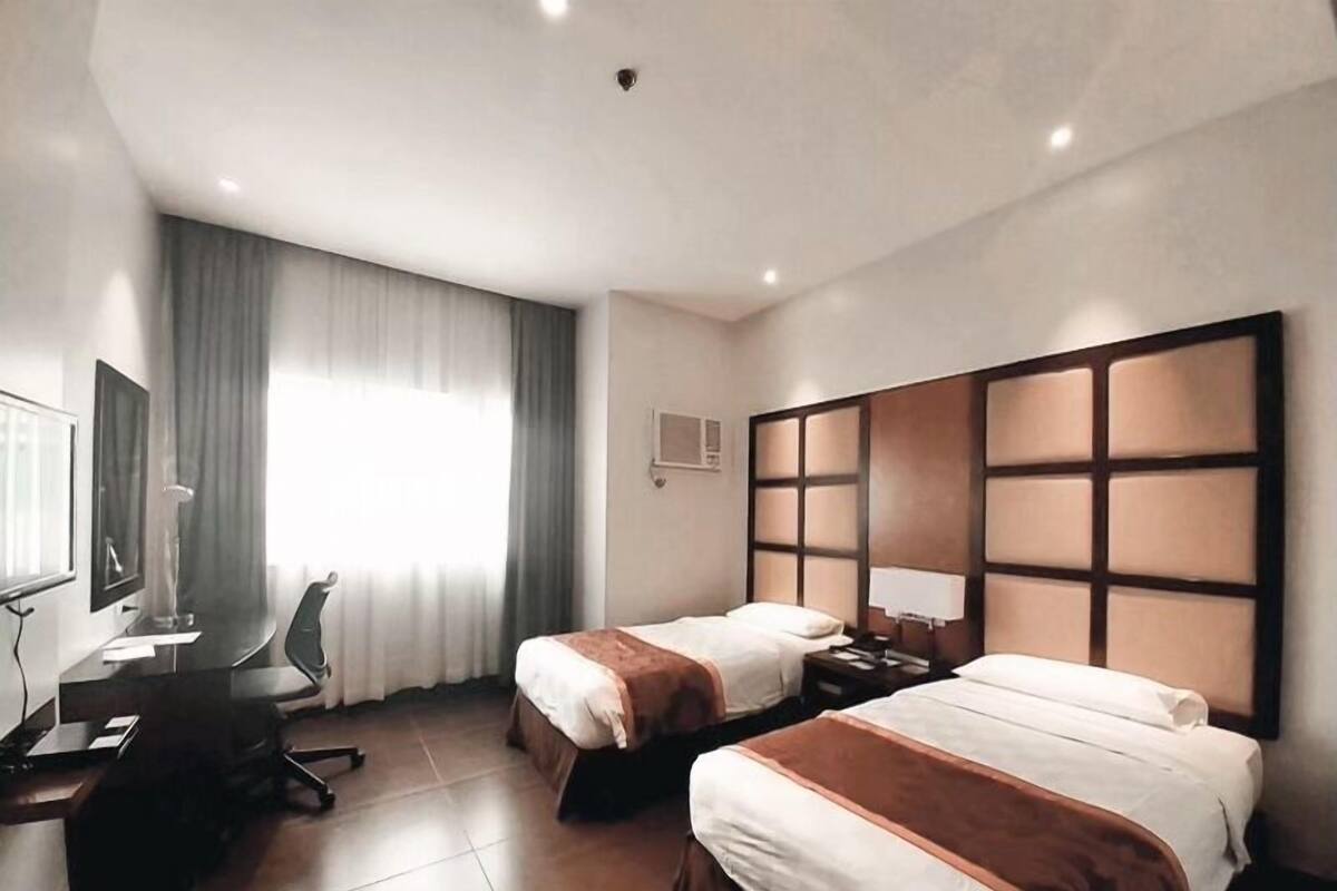 A hotel room with two beds, a desk, a chair, and a large window with curtains.