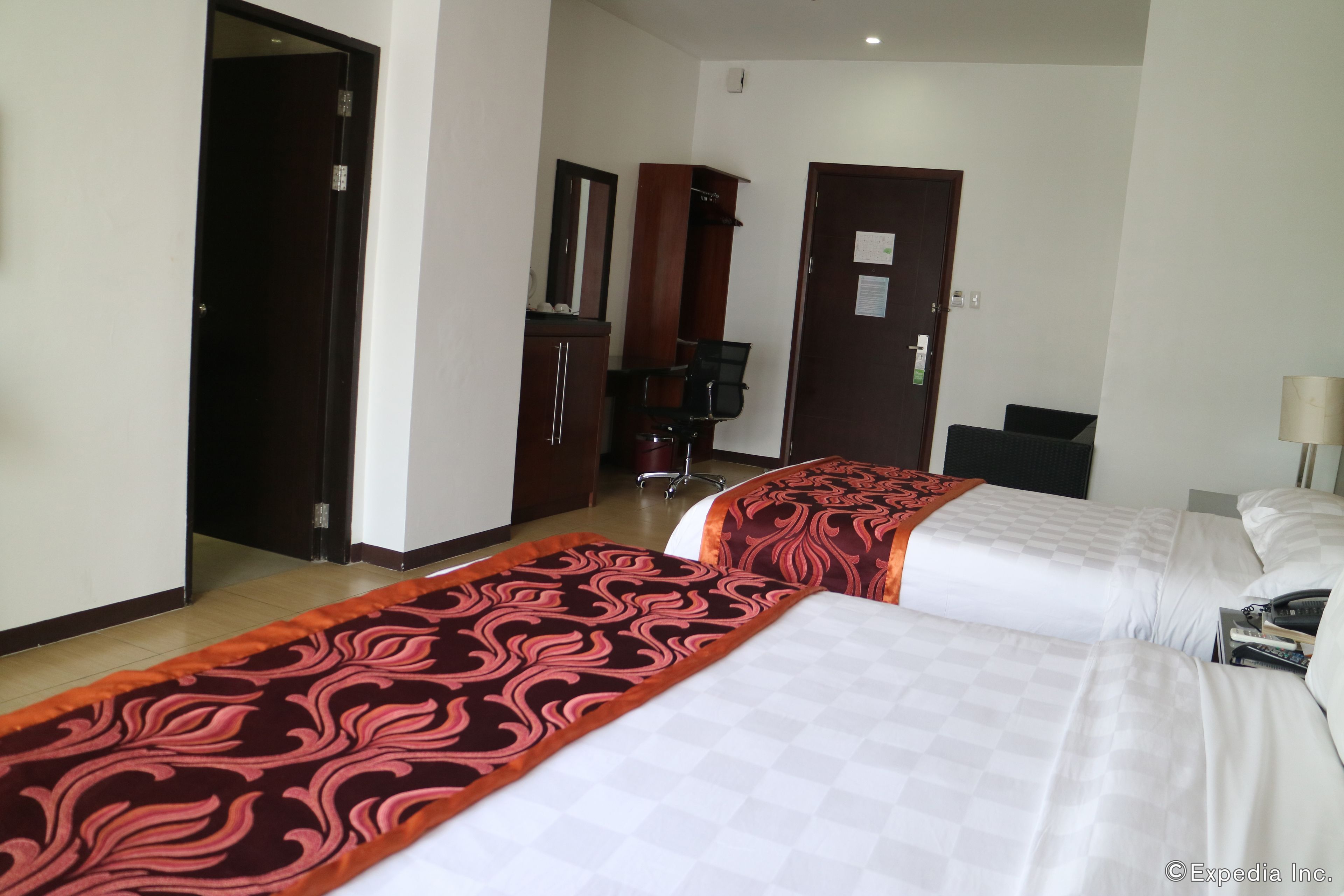 A hotel room with two beds, a desk, a chair, and a wardrobe.