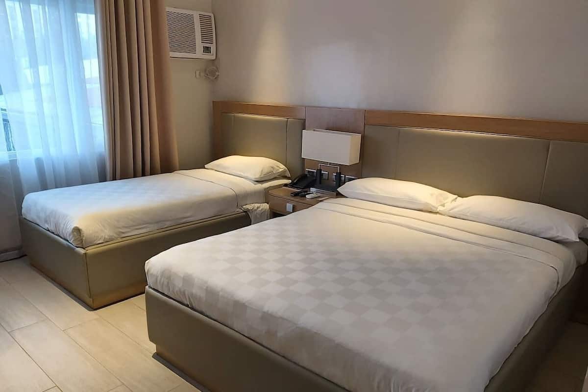 A hotel room with two beds, a bedside table with a lamp, and a window with curtains.