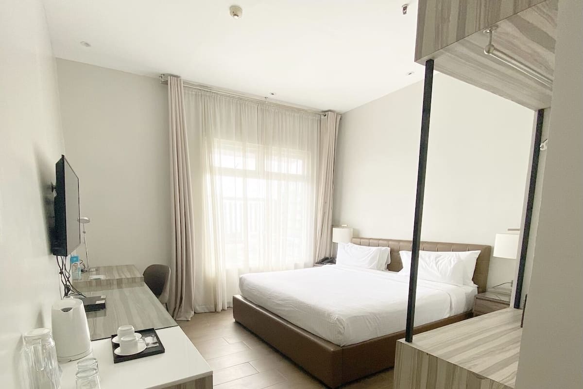 A hotel room with a bed, a bed, a desk, a chair, a mirror, and a window with curtains.