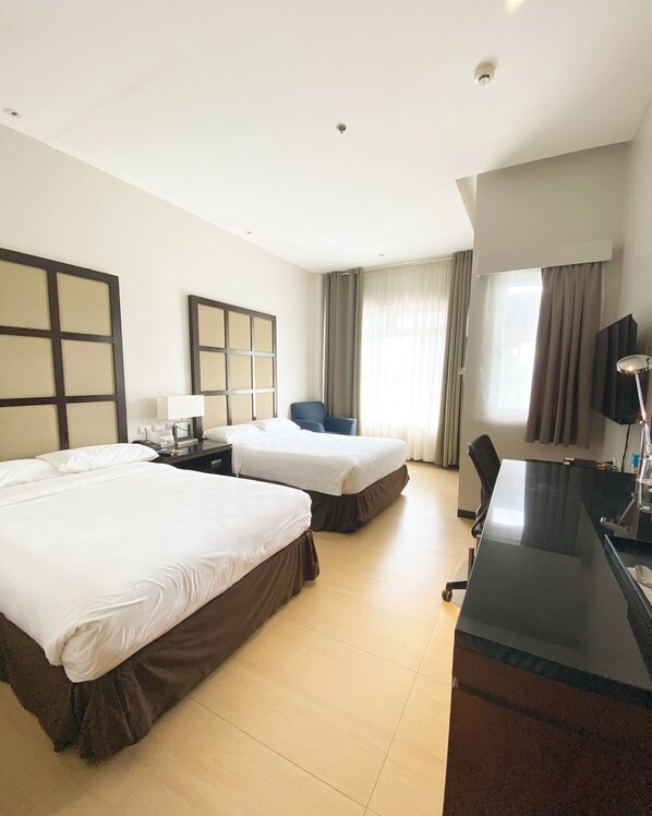 A hotel room with two beds, a desk, a chair, a TV, and a window with curtains. - Avenue Suites Hotel (Bacolod)