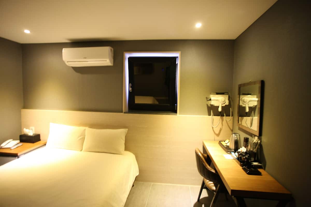 A hotel room with a bed, bedside table, desk, chair, and a window with a view.