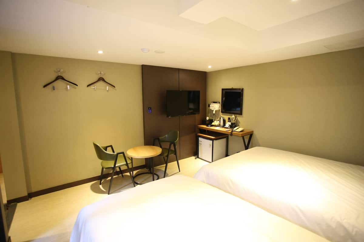A hotel room with two beds, a desk with a chair, a TV, and a small refrigerator.