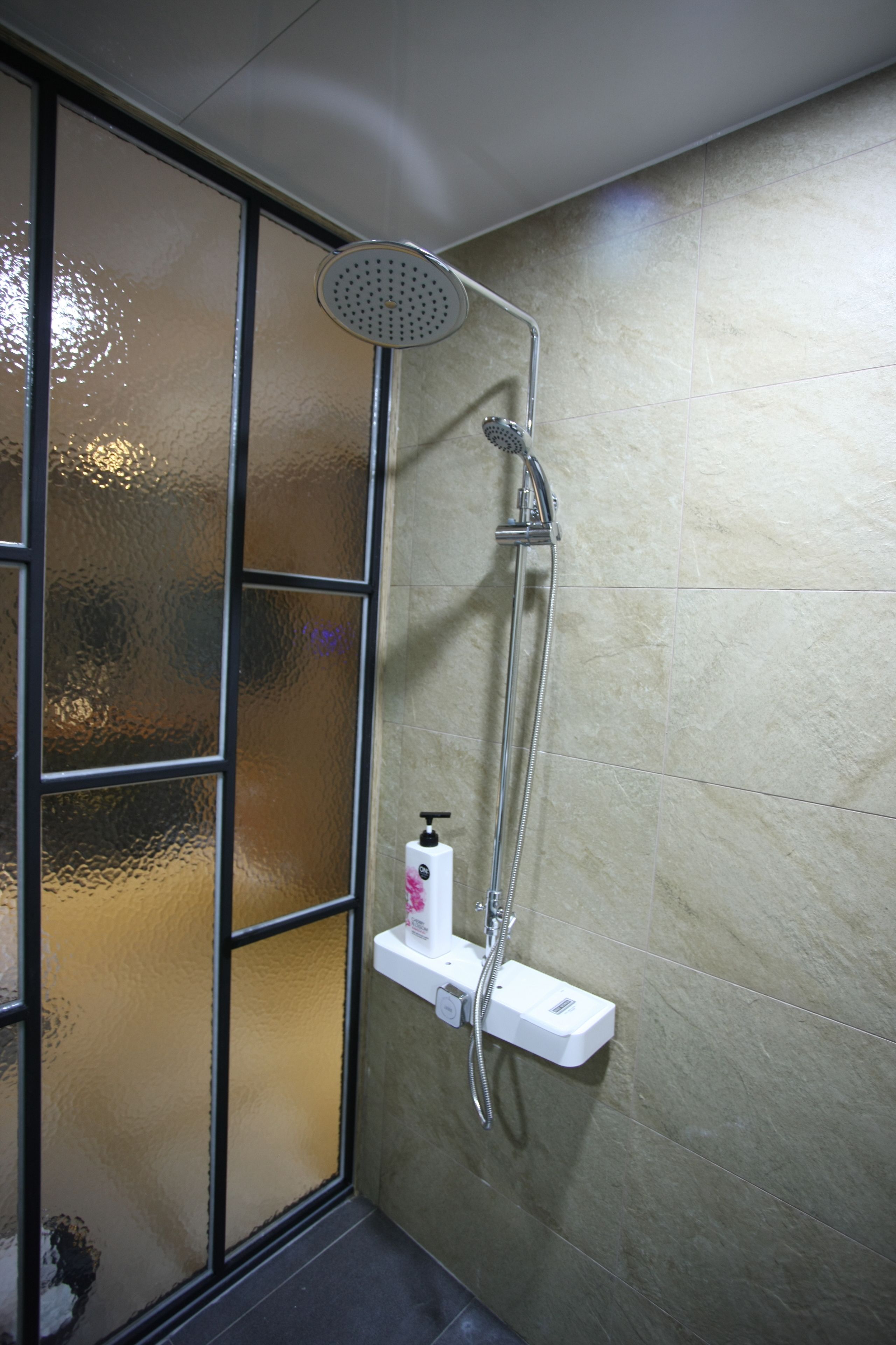 Área de chuveiro com chuveiro manual e painel de controle fixado na parede.