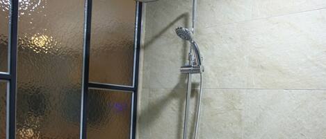 Área de chuveiro com chuveiro manual e painel de controle fixado na parede.