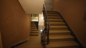 Un escalier avec une rampe, des marches recouvertes de moquette et un mur en pierre d’un côté.