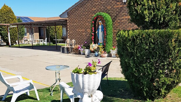 A garden with a statue, colorful flowers, and outdoor seating. - Maria Motel (Moree)