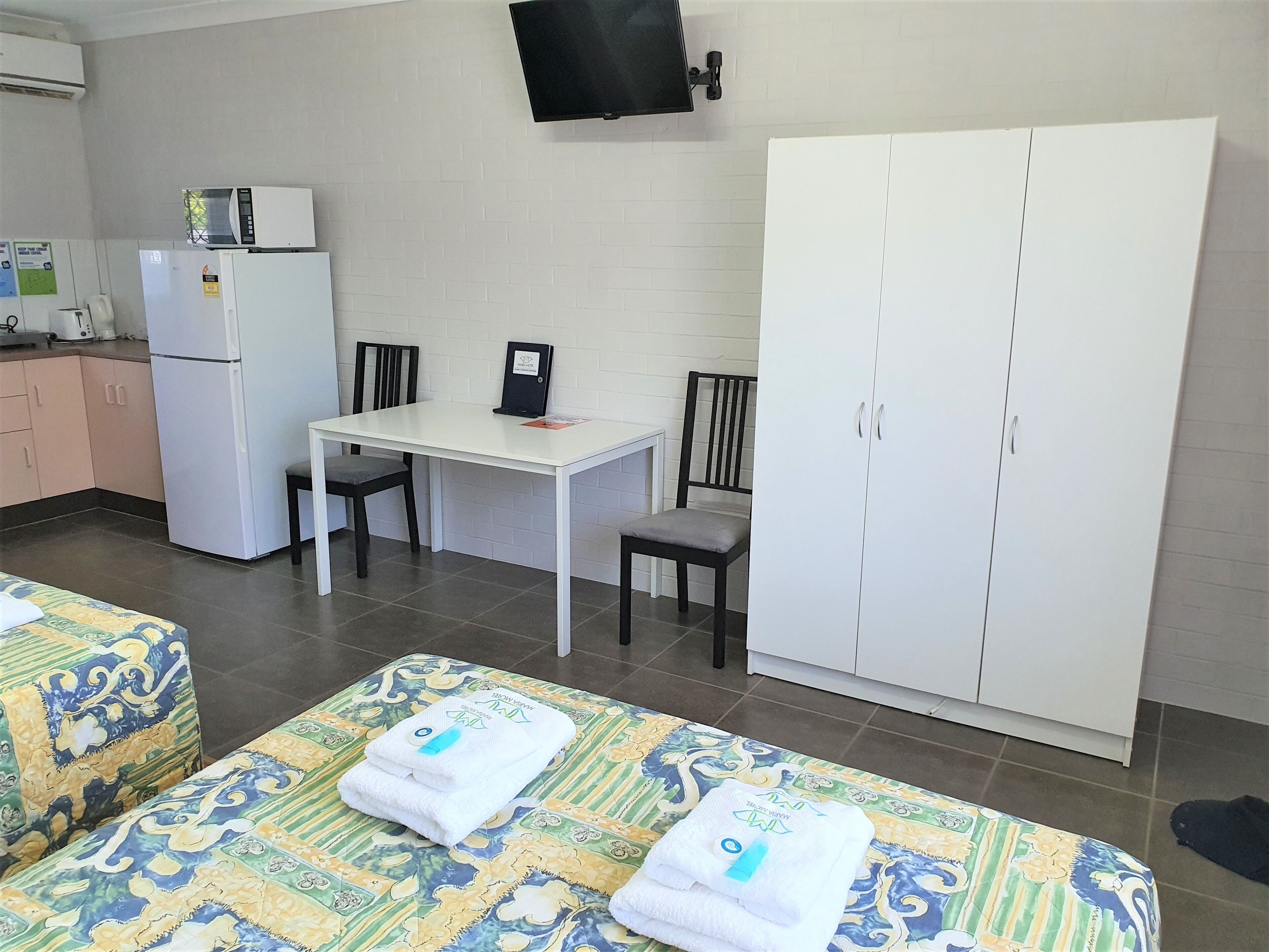 Une chambre d’hôtel équipée d’un lit, d’un bureau, d’une chaise, d’une armoire, d’une télévision et d’un réfrigérateur.
