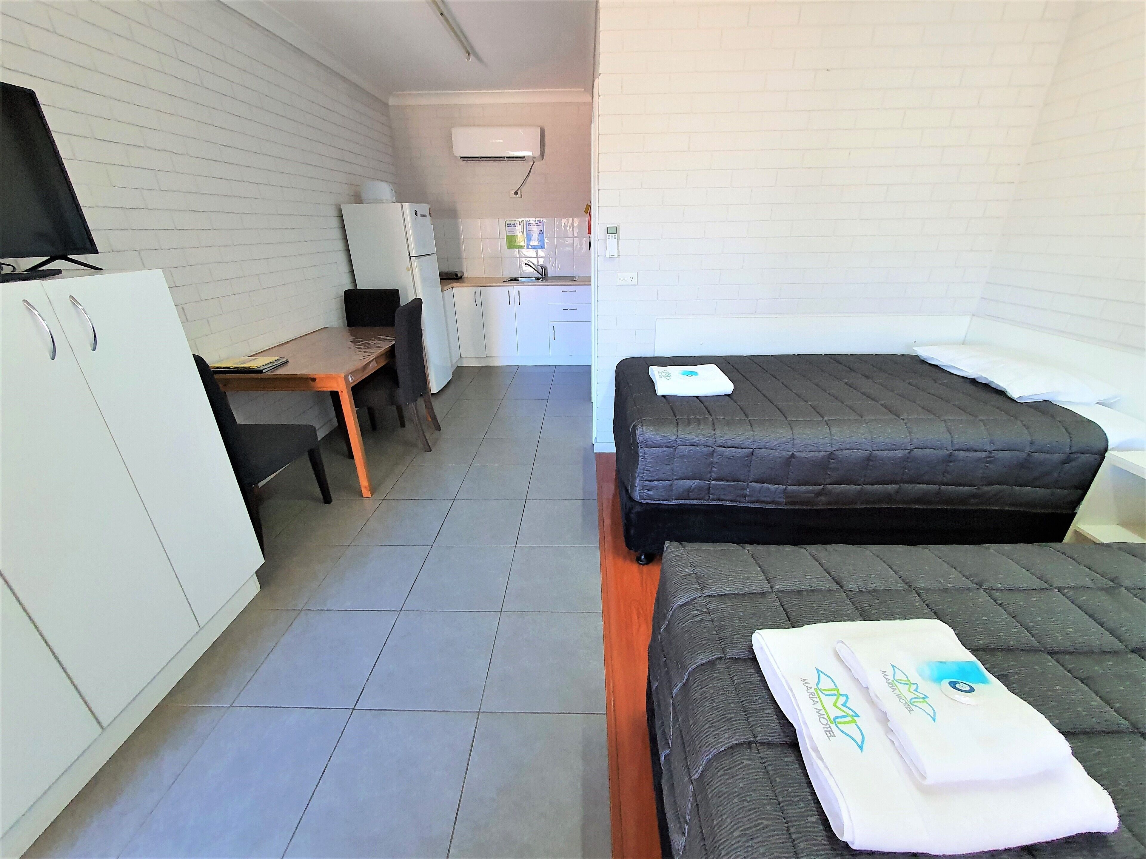 A compact hotel room with a bed, a desk, a chair, a TV, and a kitchenette.