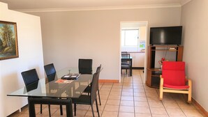 A dining area with a glass table and chairs, a red chair, a television on a wooden stand, and a painting on the wall. - Maria Motel (Moree)