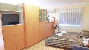 A bedroom with a bed, a sofa, a TV on a cabinet, and a window with curtains. - Maria Motel (Moree)