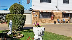 A Maria Hotel with a well-maintained garden featuring a statue, colorful flowers, and a neatly trimmed hedge. - Maria Motel (Moree)