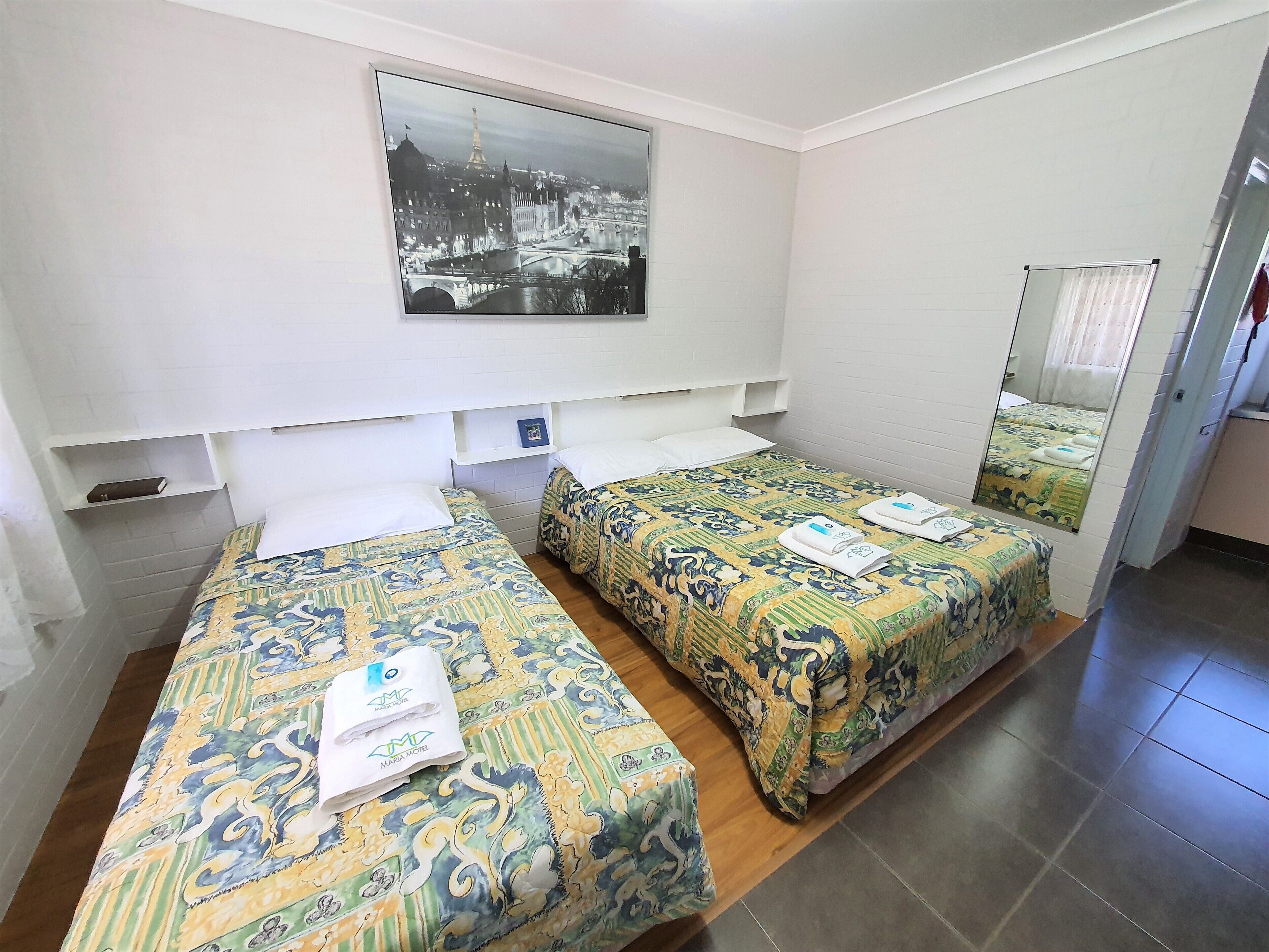 Ein Hotelzimmer mit zwei Betten, einem großen Spiegel und einem Stadtbild an der Wand.