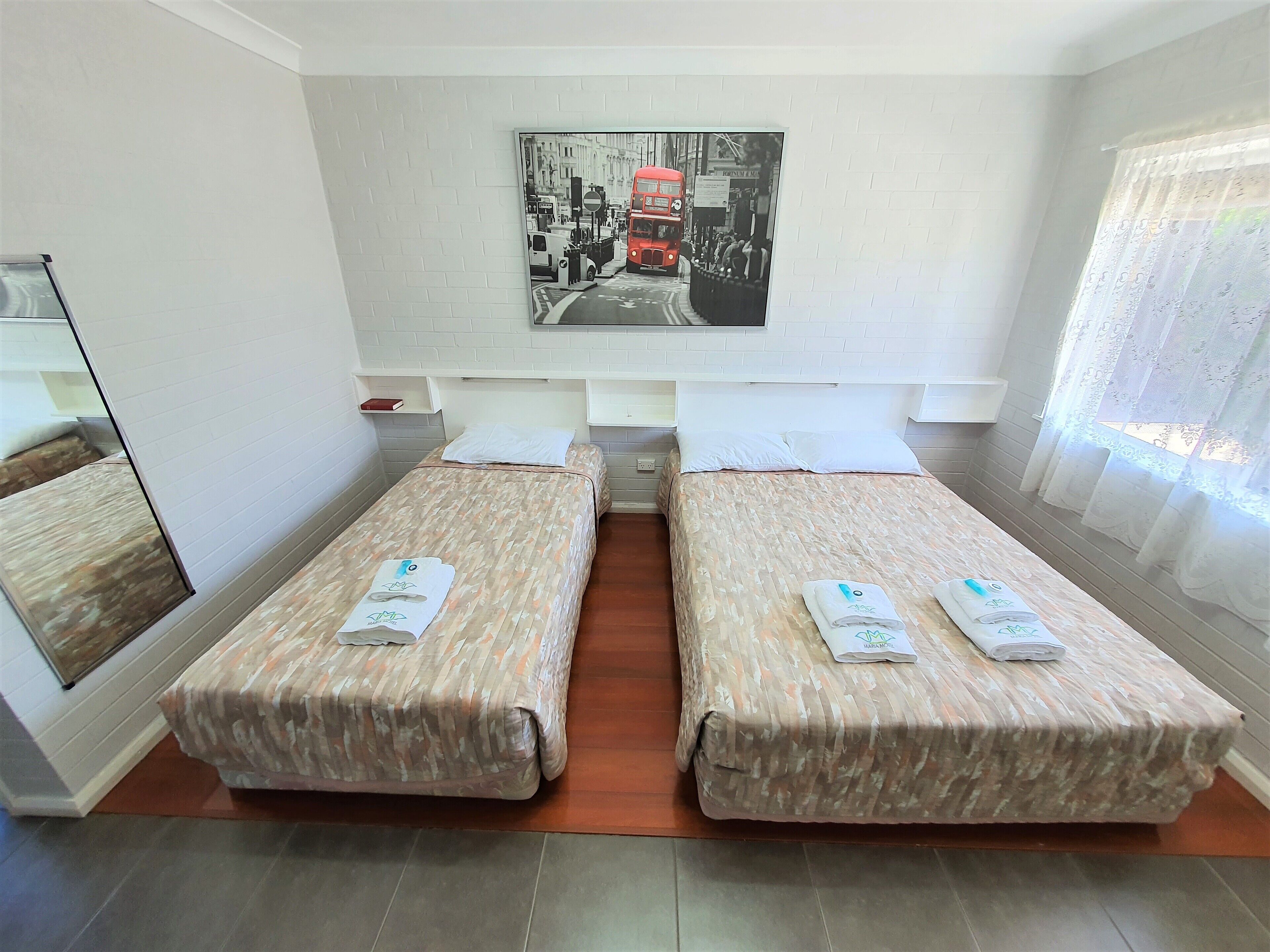 Une chambre d’hôtel avec deux lits simples, une grande fenêtre avec des rideaux légers, un tableau accroché au mur et une petite table de chevet.