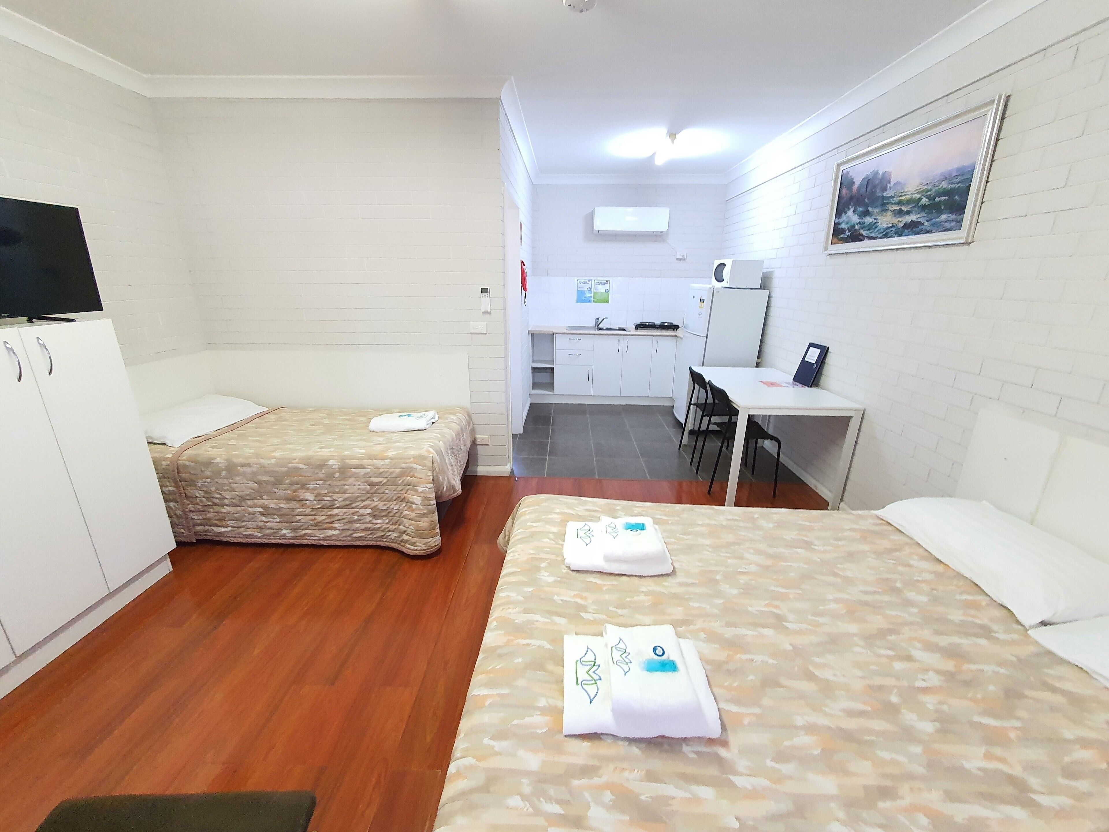 Une chambre avec deux lits, un bureau, une chaise et un coin cuisine.