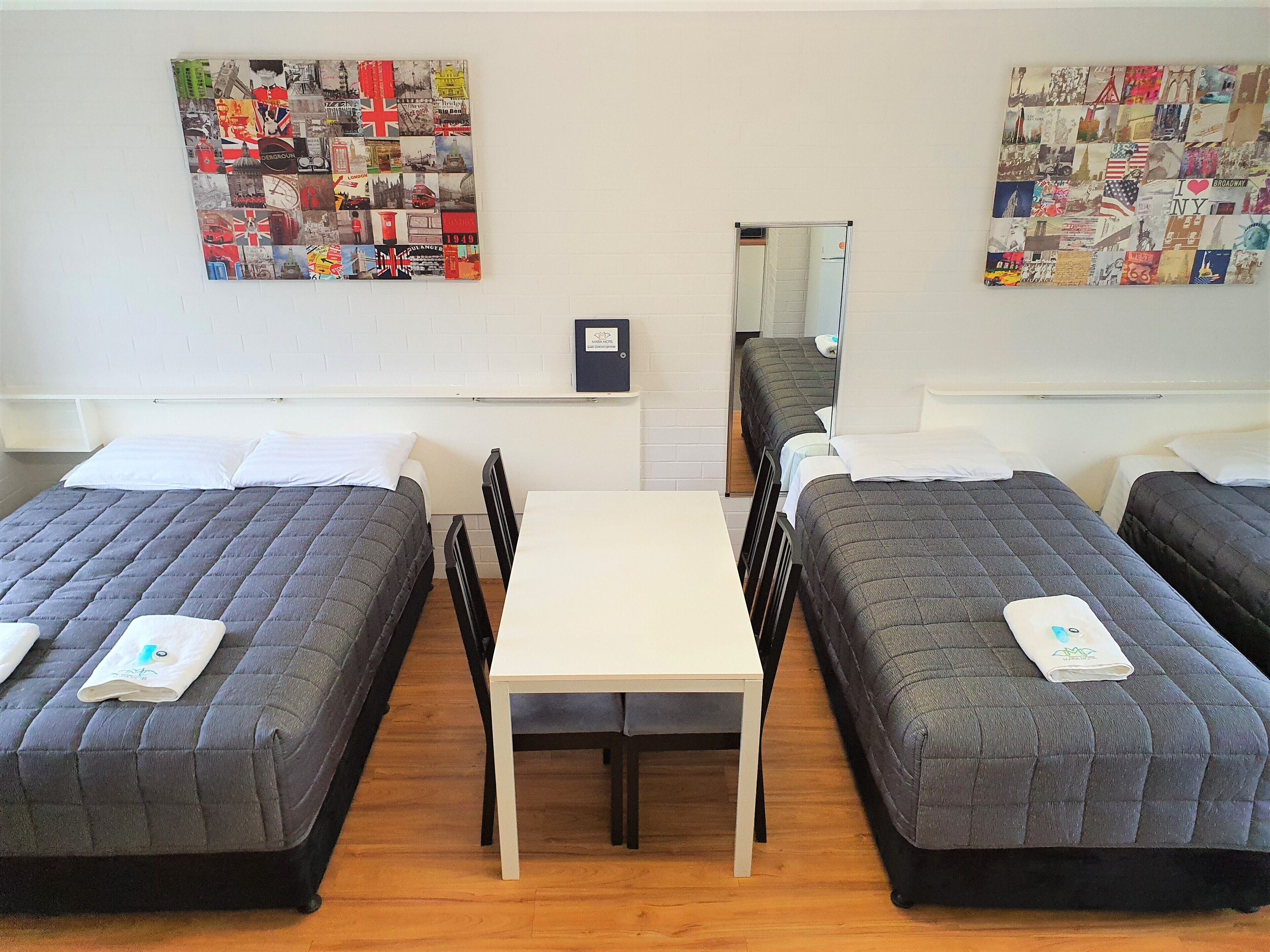 A hotel room with two single beds, a small table, and a mirror.