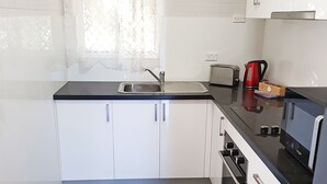 A compact kitchen with white cabinets, a black countertop, a sink, a toaster, a kettle, and an oven. - Maria Motel (Moree)
