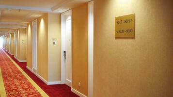 A hotel hallway with a red carpet, doors, and a sign indicating room numbers.