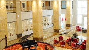 Un lobby amplio con un piano de cola, sillas rojas y una escalera que sube a un nivel superior.