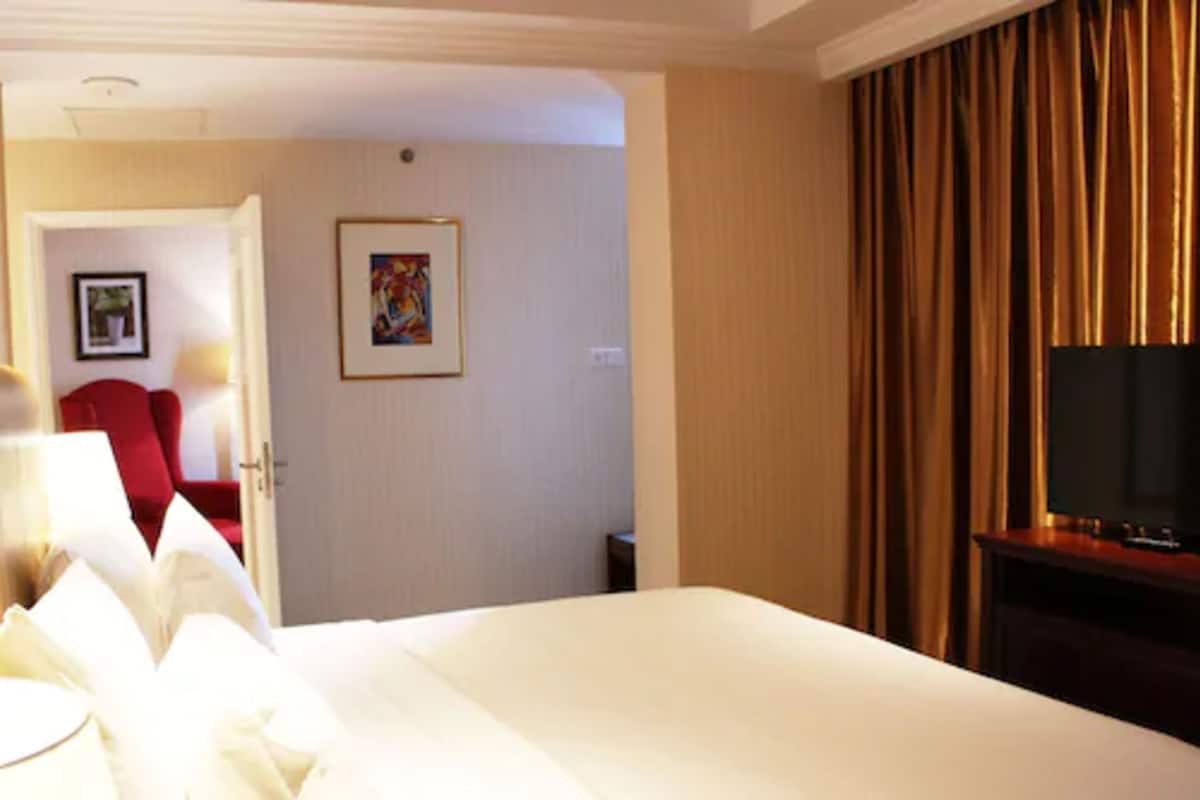 A hotel room with a large bed, a television, a red chair, and a painting on the wall.