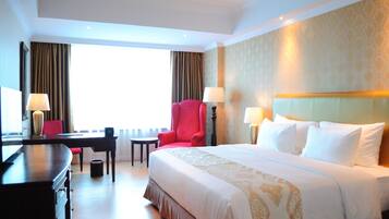A hotel room with a large bed, a desk, a red armchair, and a window with curtains.