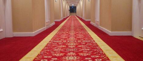 Un pasillo de hotel con alfombra roja, paredes color beige y puertas numeradas.