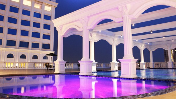 Vista nocturna de un área de piscina con columnas blancas y una piscina reflectante.