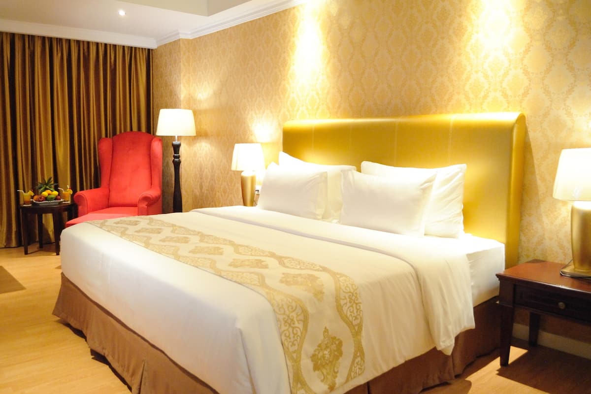 A hotel room with a large bed, a red armchair, two bedside tables with lamps, and a curtain backdrop.
