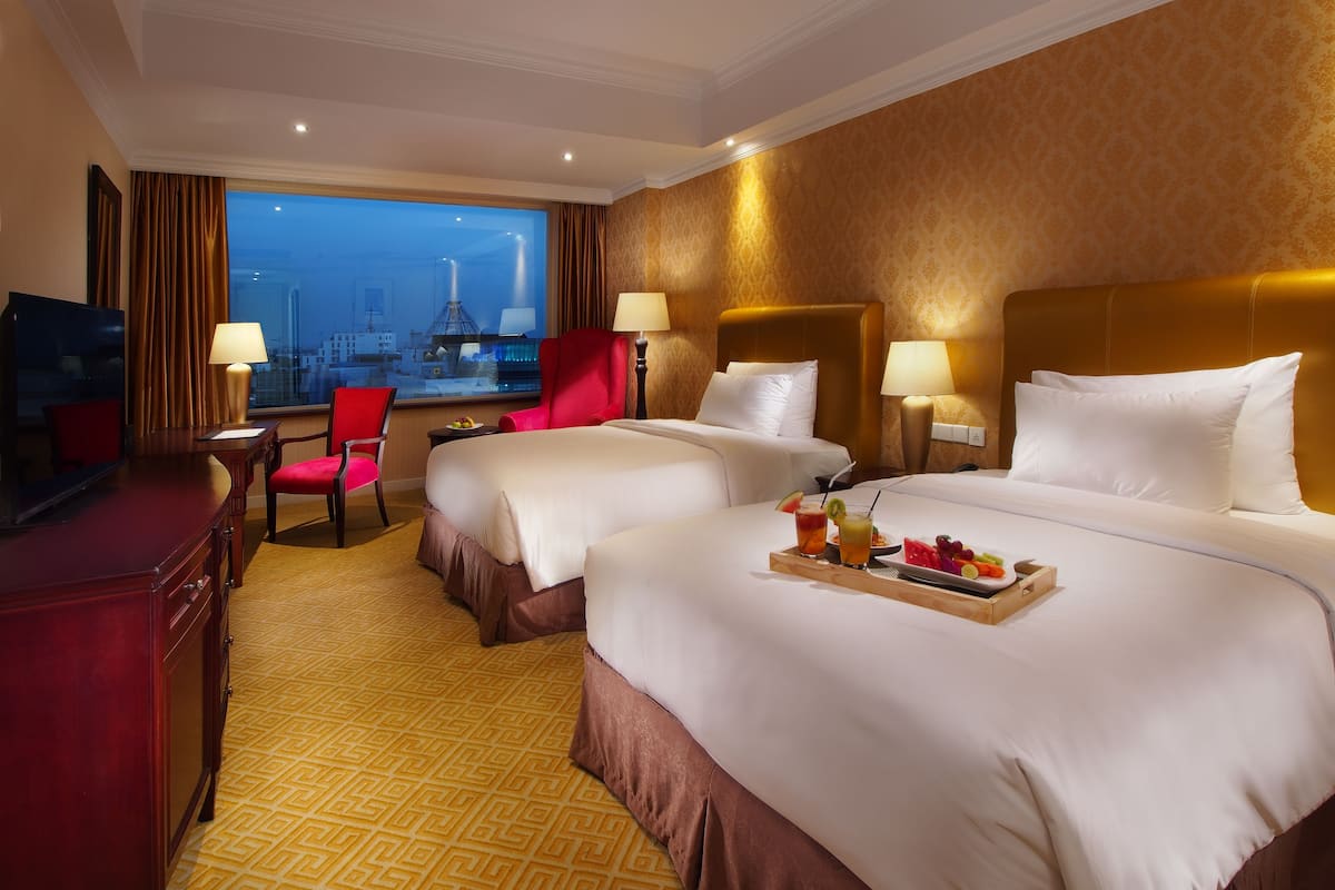 A hotel room with two beds, a desk, a TV, and a city view.