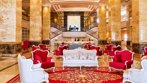 Un lobby imponente con columnas de mármol, un sofá rojo y blanco, y una escalera que conduce a un nivel superior.
