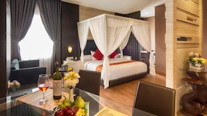 Ein Hotelzimmer mit einem Bett, einem Glastisch mit einer Weinflasche, Obst und Blumen, und Blick ins Zimmerinnere.