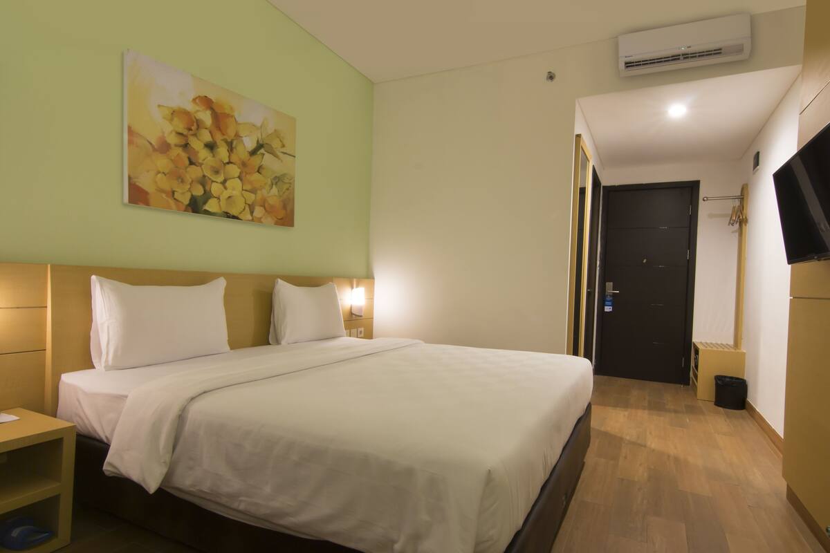 Une chambre d’hôtel avec un lit, une table de chevet, un climatiseur fixé au mur et un tableau.