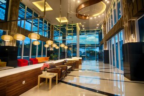 Un lobby moderno de hotel con una recepción, zona de estar y ventanas amplias.