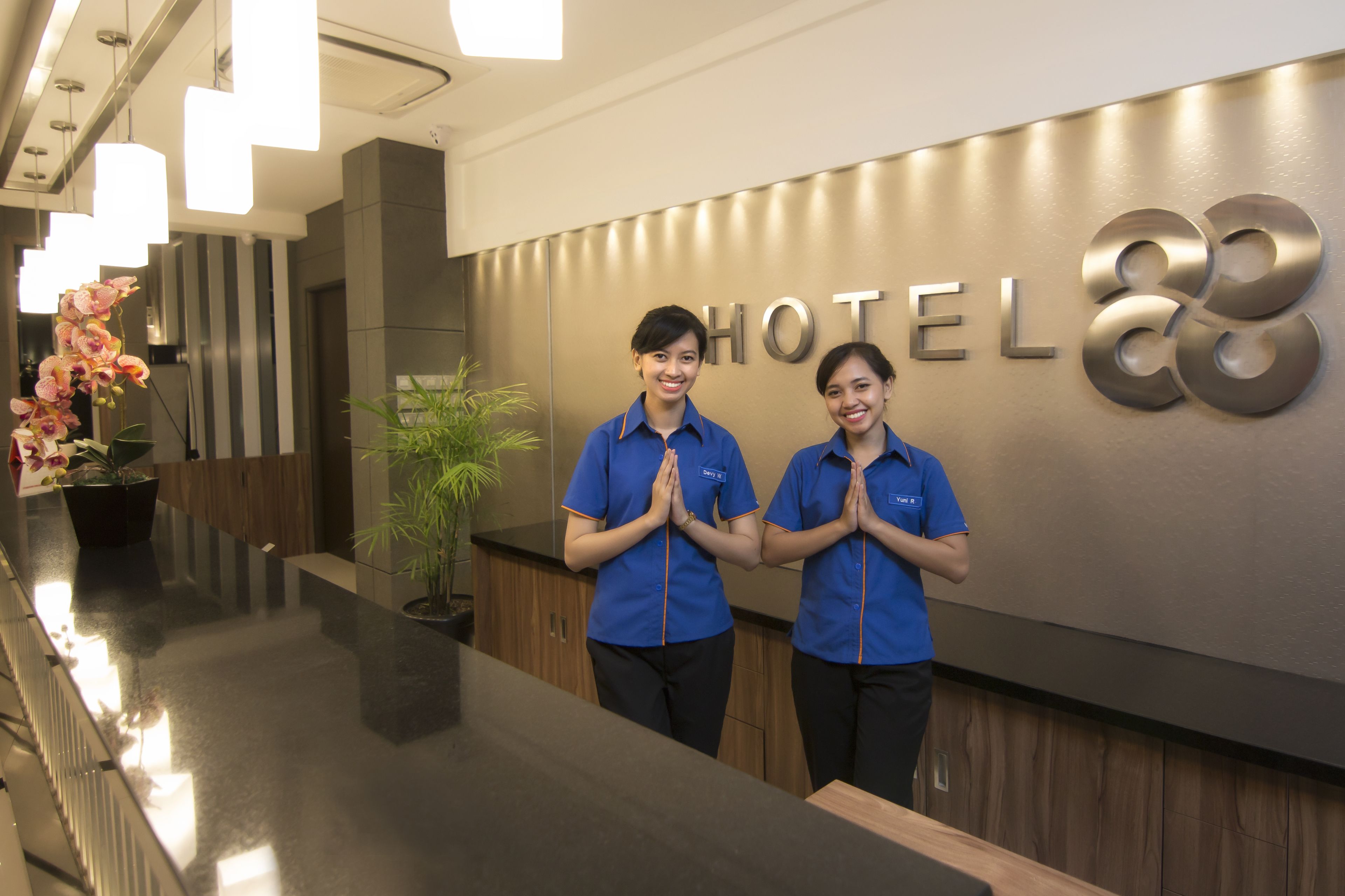 A reception desk with a 'HOTEL' sign and two staff members standing behind it.