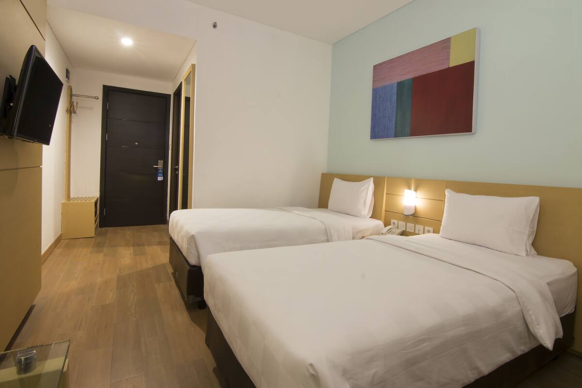 Une chambre d’hôtel avec deux lits, un téléviseur à écran plat fixé au mur et un tableau au-dessus des lits.